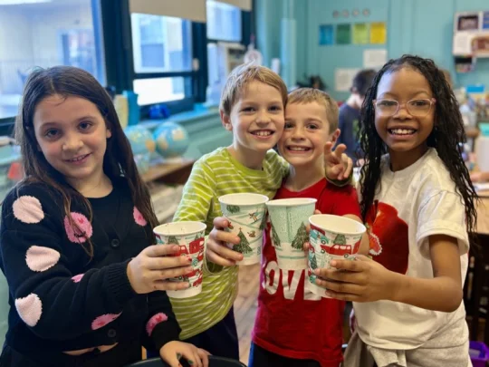 Four Connors students in a classroom raising winter-themed cups for a toast