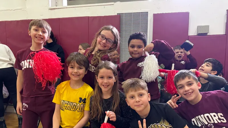 Connors kids in maroon spiritwear crowded together with red and white pom-poms in the gym