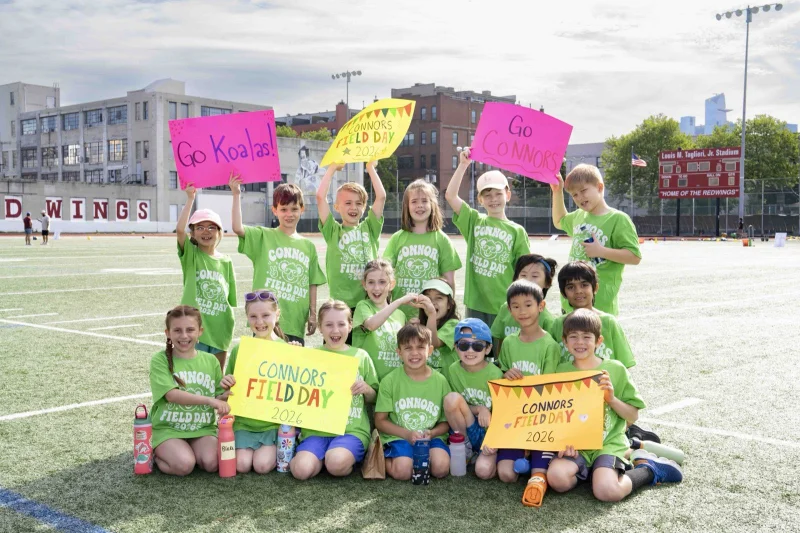 Connors students in green Field Day t-shirts holding 'Go Koalas' signs on the field