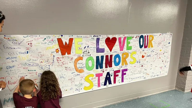 Two Connors students signing a giant hand-colored We Love Our Connors Staff banner