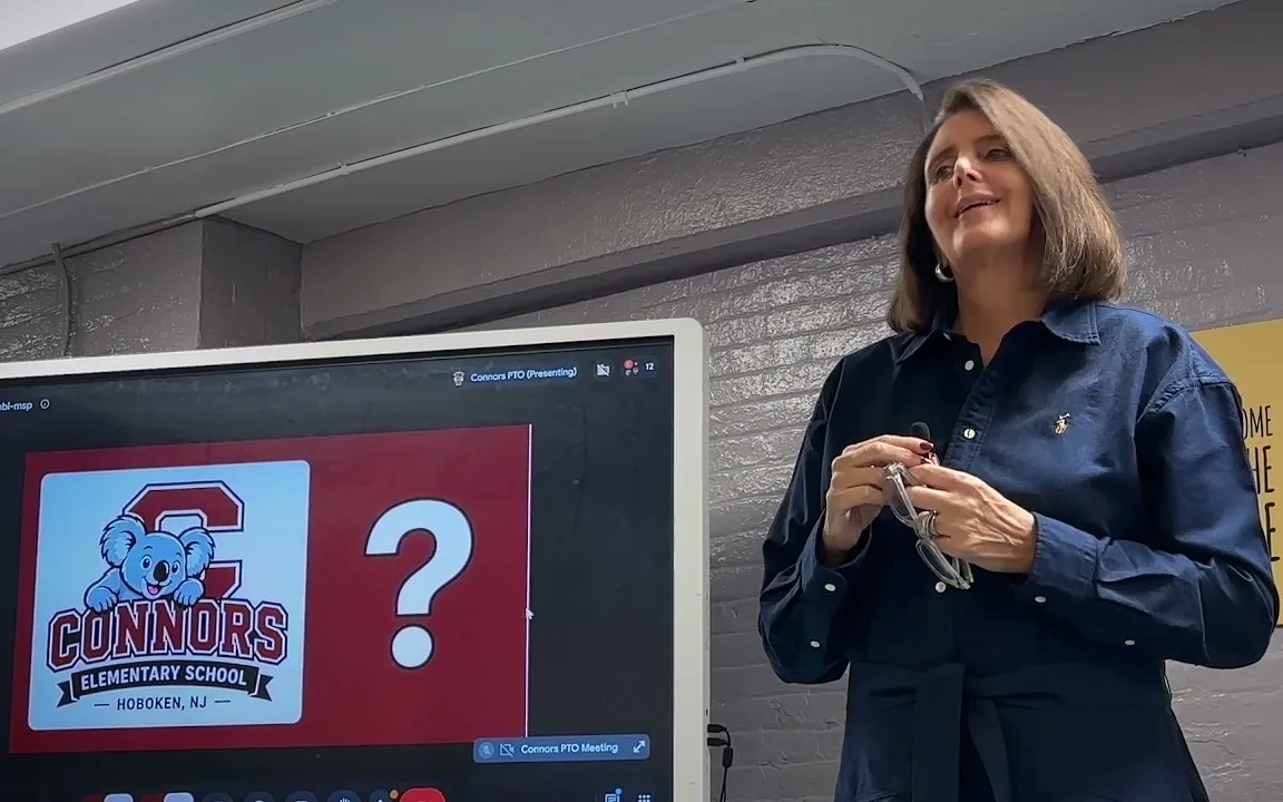 Dr. Christine Johnson smiling as she speaks to Connors parents in the cafeteria, the Connors koala logo on the screen beside her