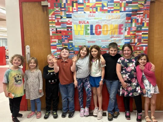 Connors students in front of a Welcome banner covered in flags from around the world